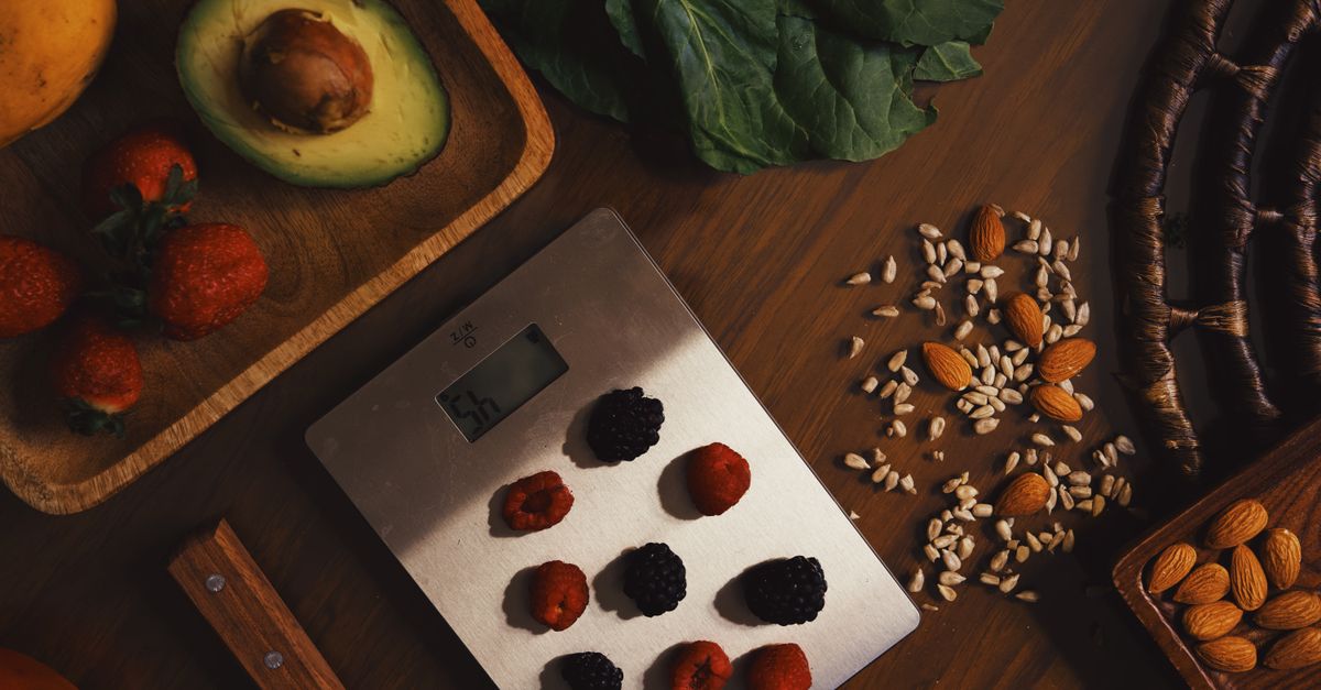 Top view of composed raw almond with seeds and avocado on table with berries on scales for cooking healthy dish